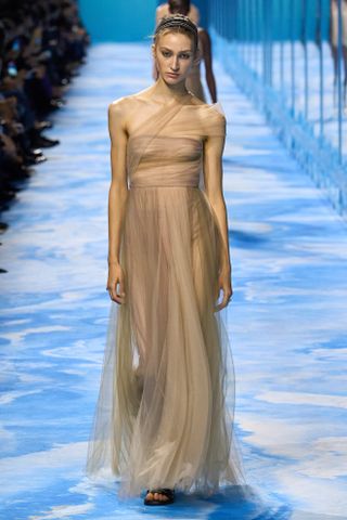 A woman wears a gold one shoulder gown at the Dior S/S 25 show.