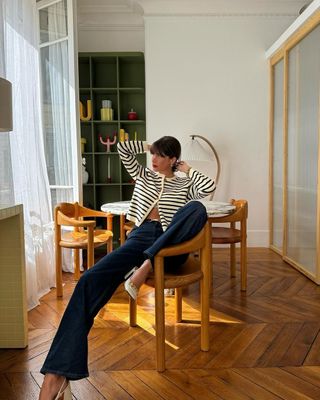 French influencer Juliesfi in apartment in flared jeans and Breton striped cardigan.