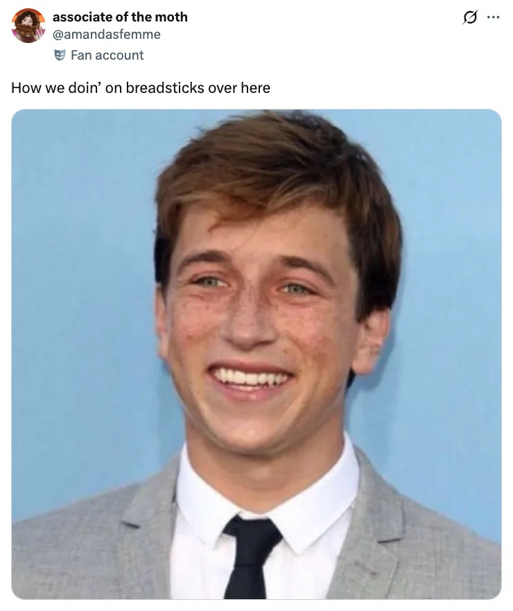 Skyler Gisondo smiling in a suit and tie, with text overlay saying, "How we doin' on breadsticks over here."