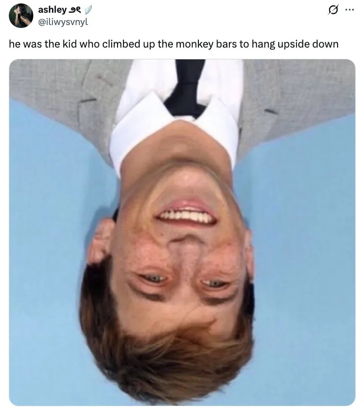 Upside-down Skyler Gisondo in a suit smiling, with caption about climbing monkey bars and hanging upside down