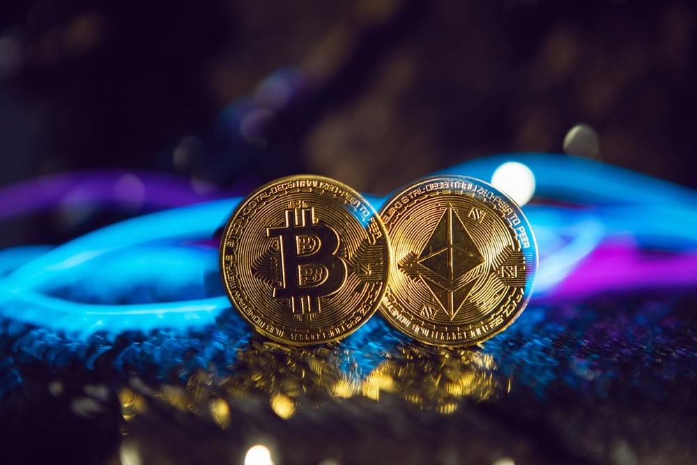 two gold iron coins ethereum and bitcoin on a shiny silver background. blue and pink wire cyberpunk in future