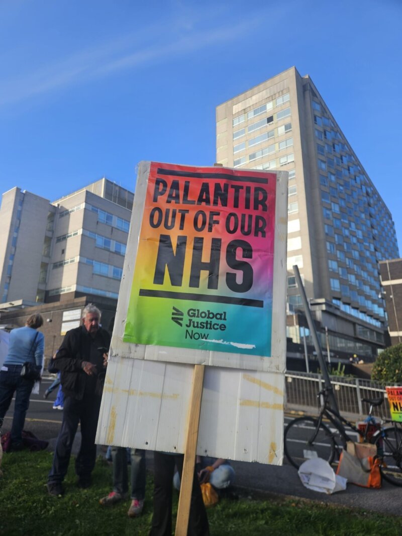 A photo of a protest sign being held up at a demonstration, with the words "PALANTIR OUT OF OUR NHS" on it