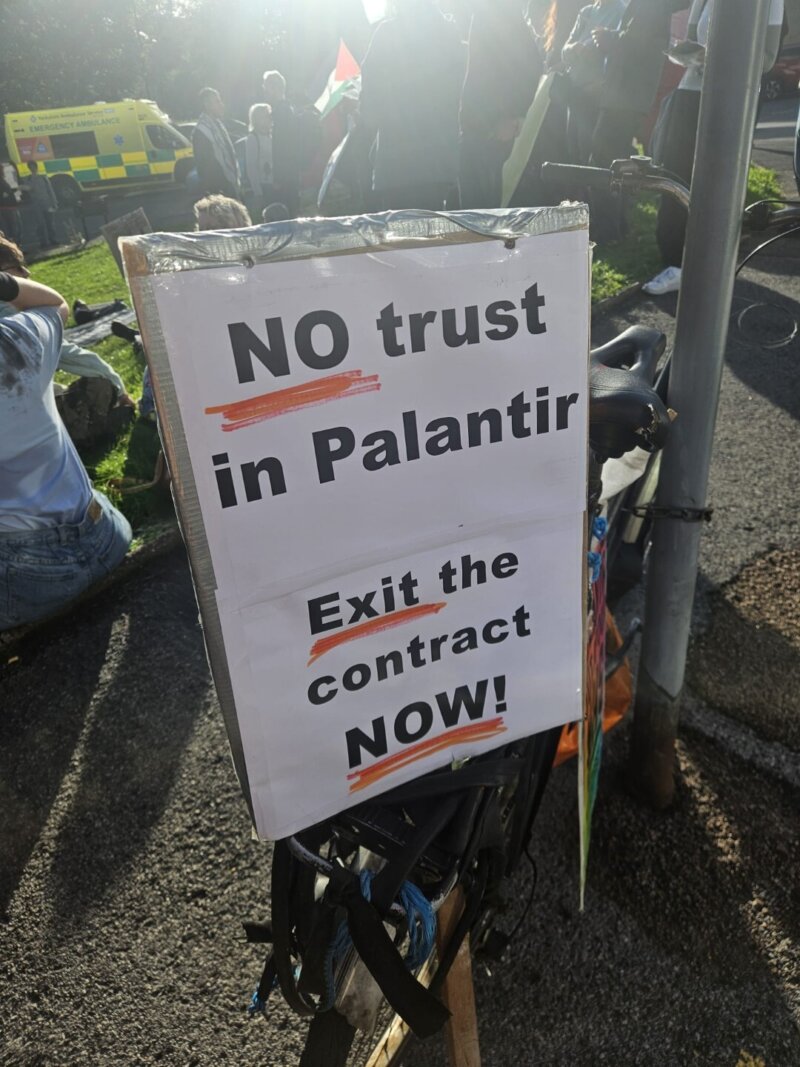 A photo of a protest sign at a demonstration with the words "NO trust in Palantir. Exit the contract NOW!"