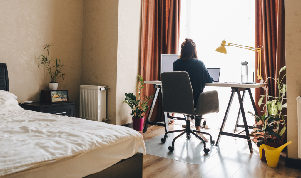 Person working remotely at a desk in a bedroom, illustrating hybrid work.