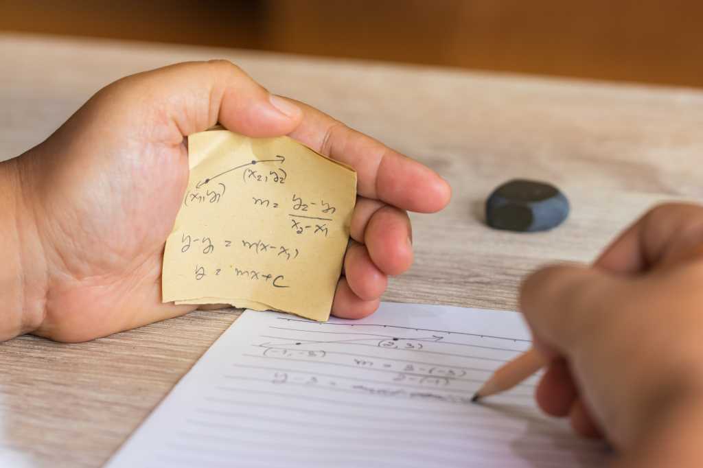 OpenAI reports three new incidents of misalignment Man using formula math sheet to cheat on test. Hand of university student holding pencil doing math question in examination and cheating with answer piece of paper in hand