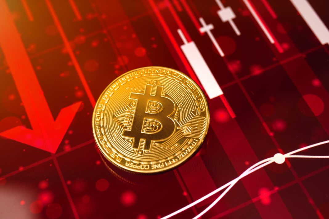 Bitcoin Drops to $80,000: Buying Opportunity or Another Crash on the Horizon? A golden Bitcoin coin is prominently displayed on a vibrant red background. Behind it, a large red arrow points downwards, symbolizing a market decline, alongside white candlestick chart bars indicating a drop. Faint red bokeh lights are scattered across the dark red background, creating a sense of urgency and a negative market trend.