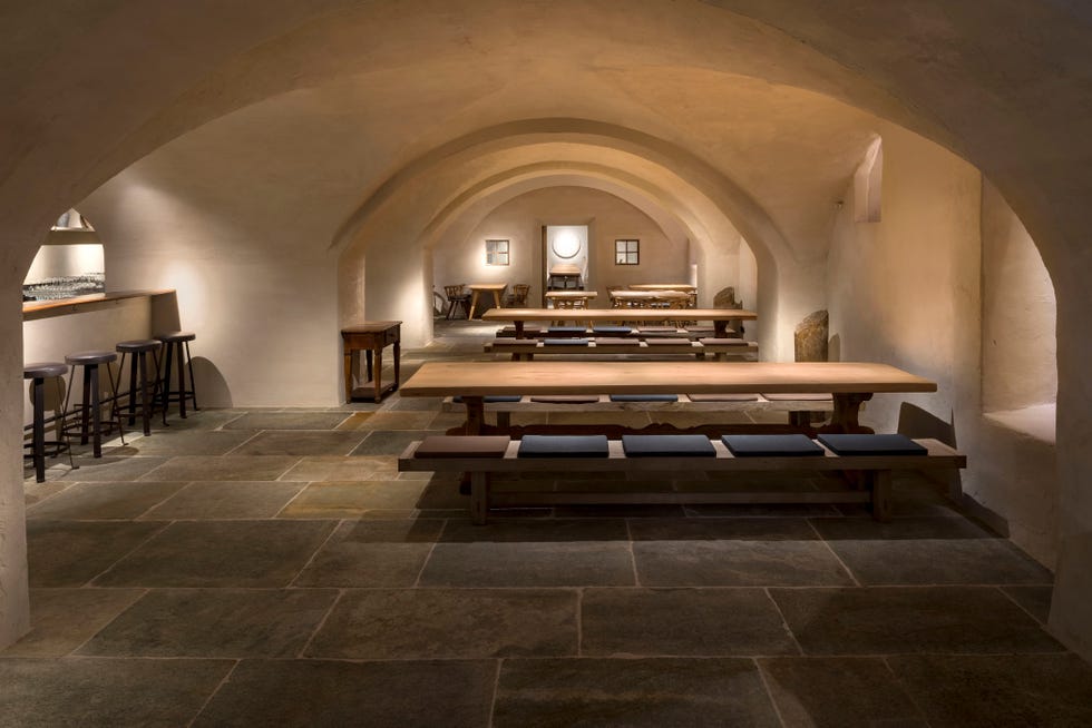 Modern dining space with wooden tables, benches, and arched ceilings in a softly lit room.