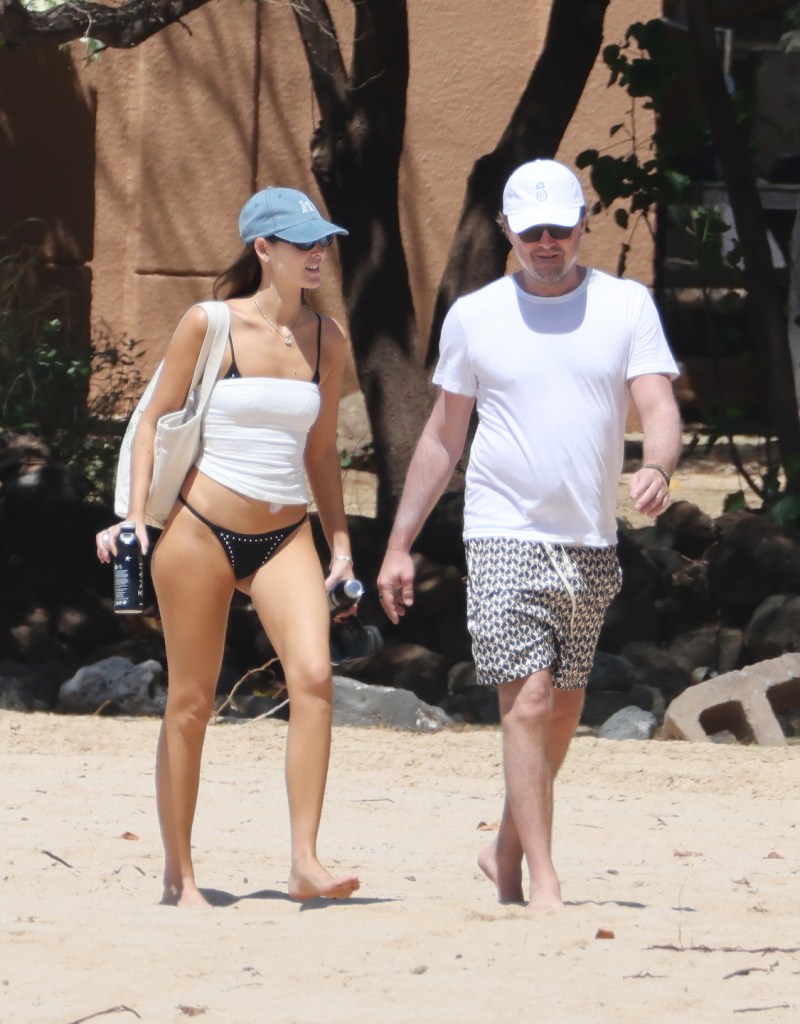 Leonardo DiCaprio and Vittoria Ceretti walking together on a sandy beach.