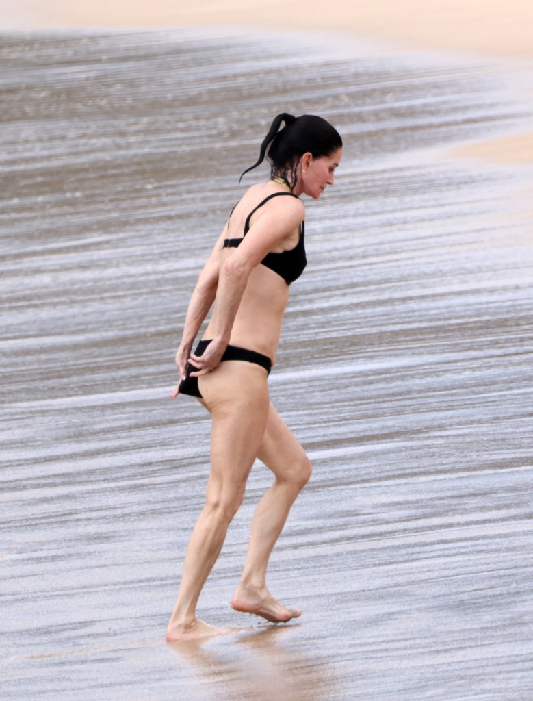 Courteney Cox wearing a black bikini on a beach in Hawaii.