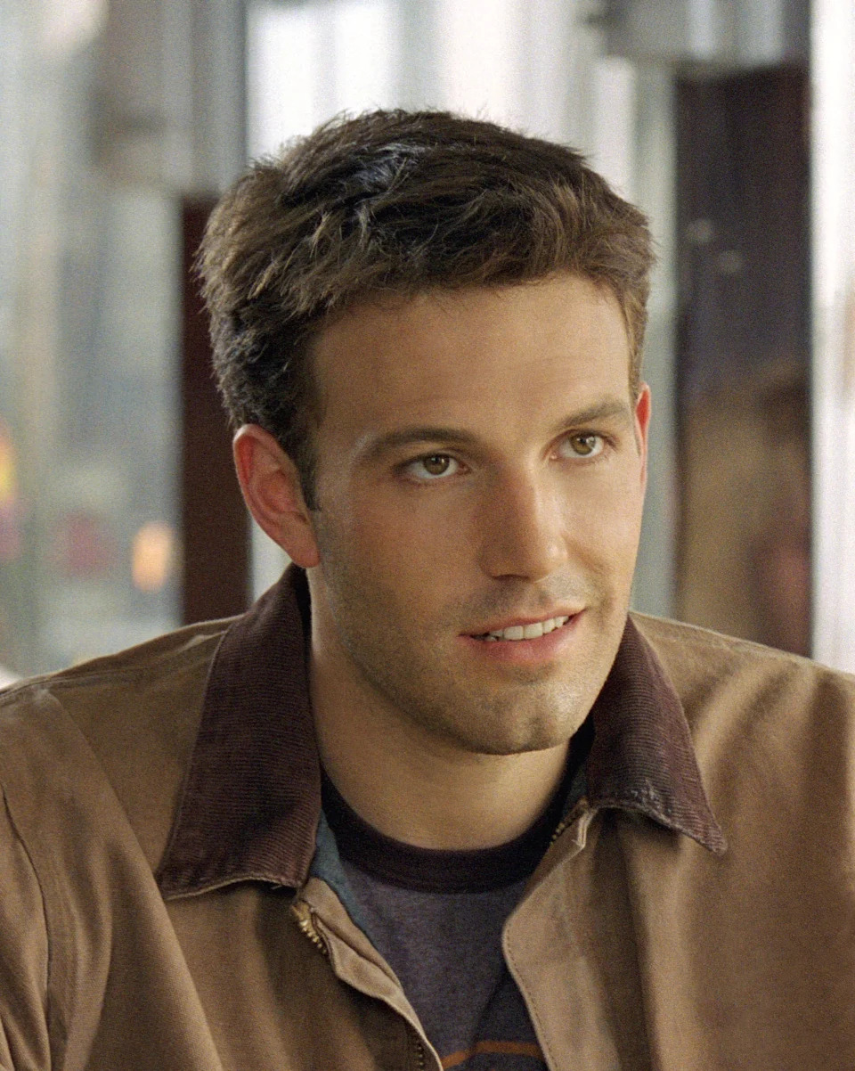 A person wearing a casual jacket and shirt is seated indoors, looking slightly to the side