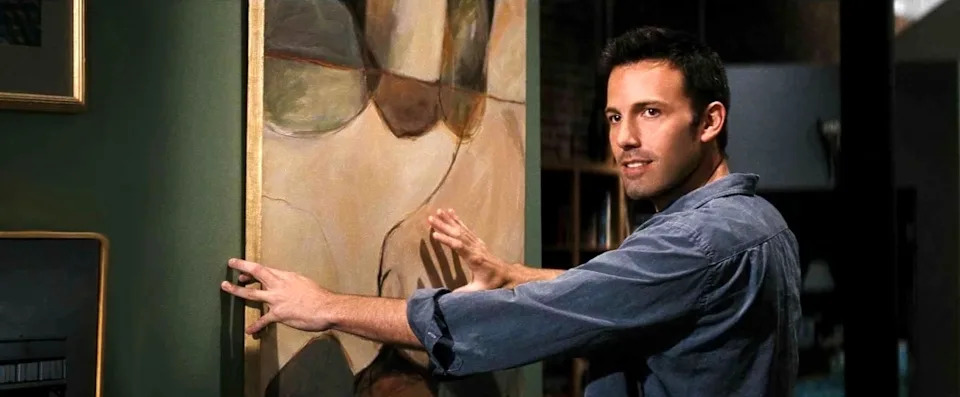 Person in casual shirt hanging abstract artwork on a wall indoors