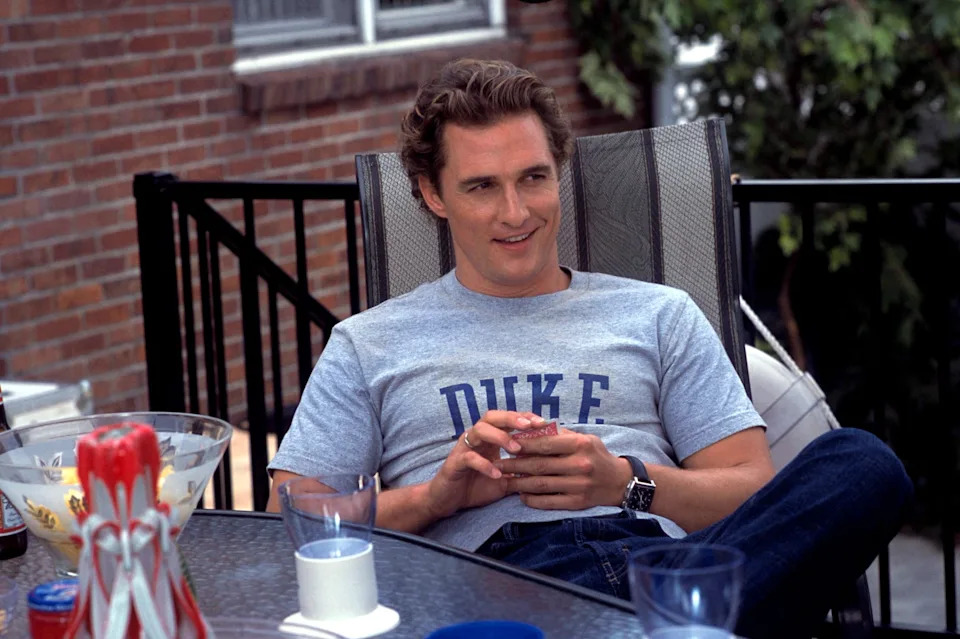 A person is relaxing outdoors on a deck chair, wearing a gray T-shirt with the word "DUKE" on it
