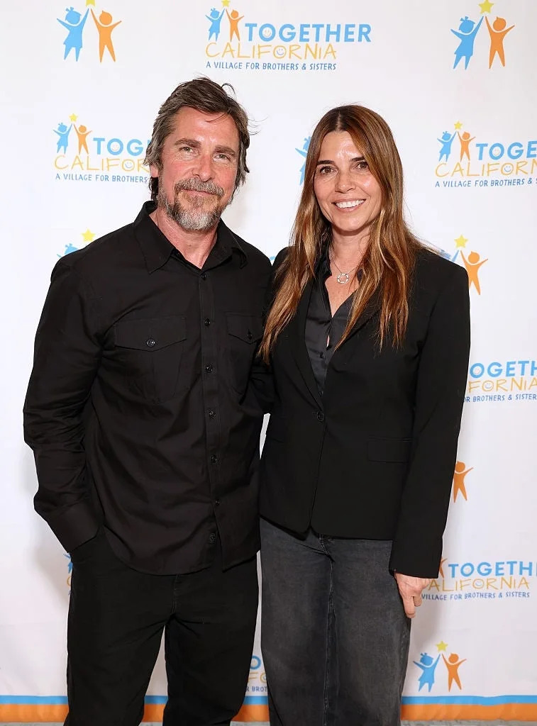 Two people smiling at a "Together California" event backdrop, dressed in smart casual outfits