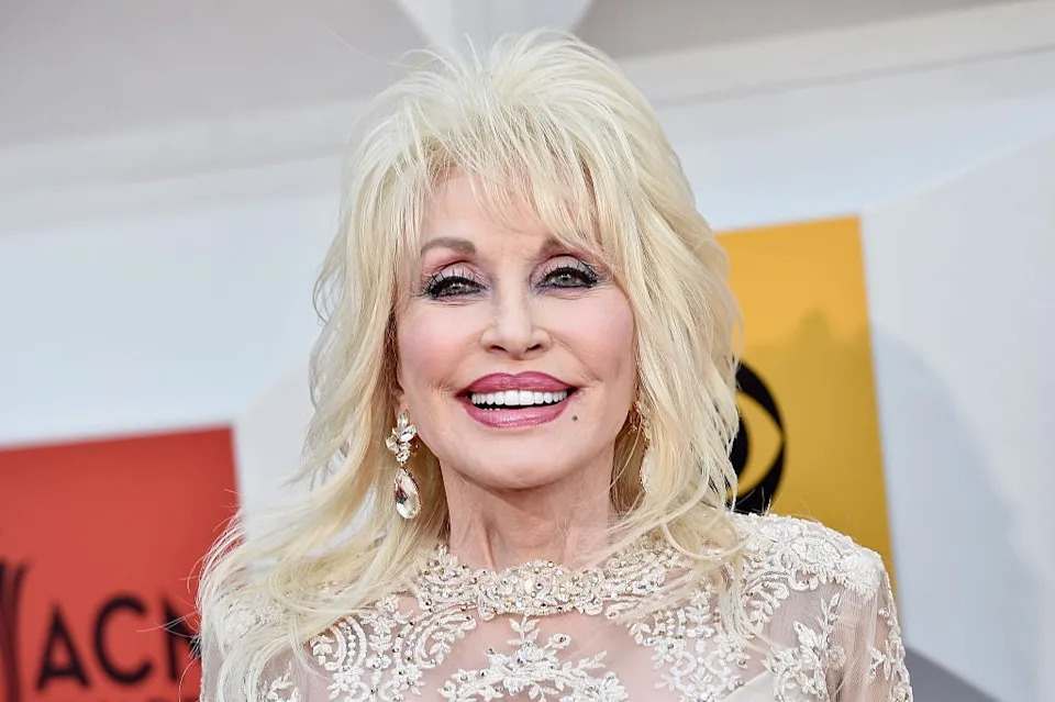 Person smiling, wearing an elegant, sparkling lace dress with intricate details, and dangling earrings