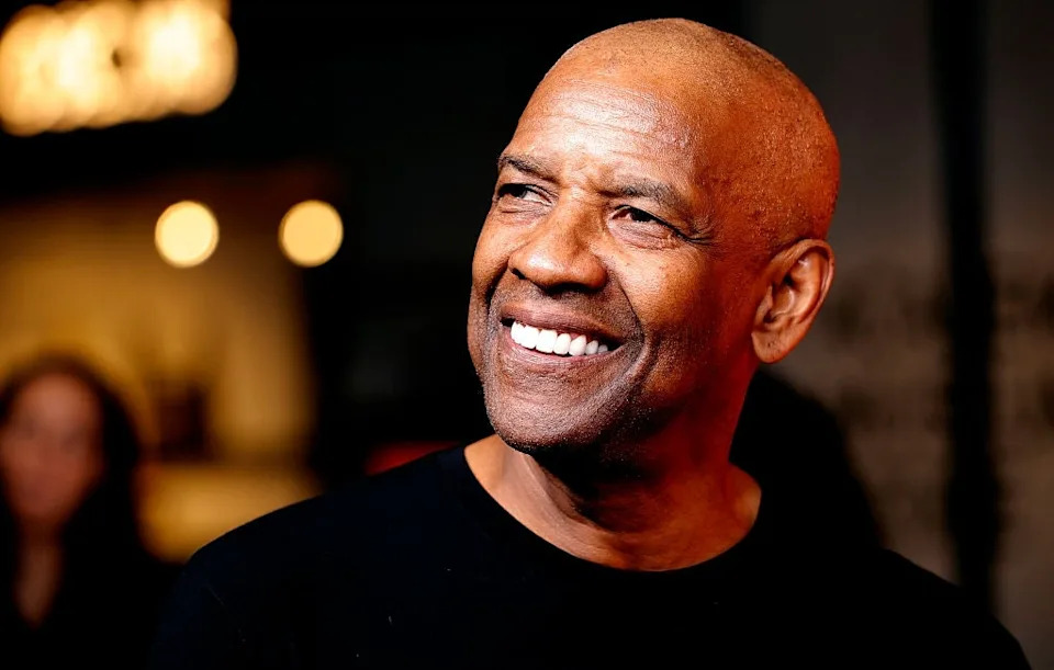 A man smiling and looking to the side, wearing a dark shirt at a public event