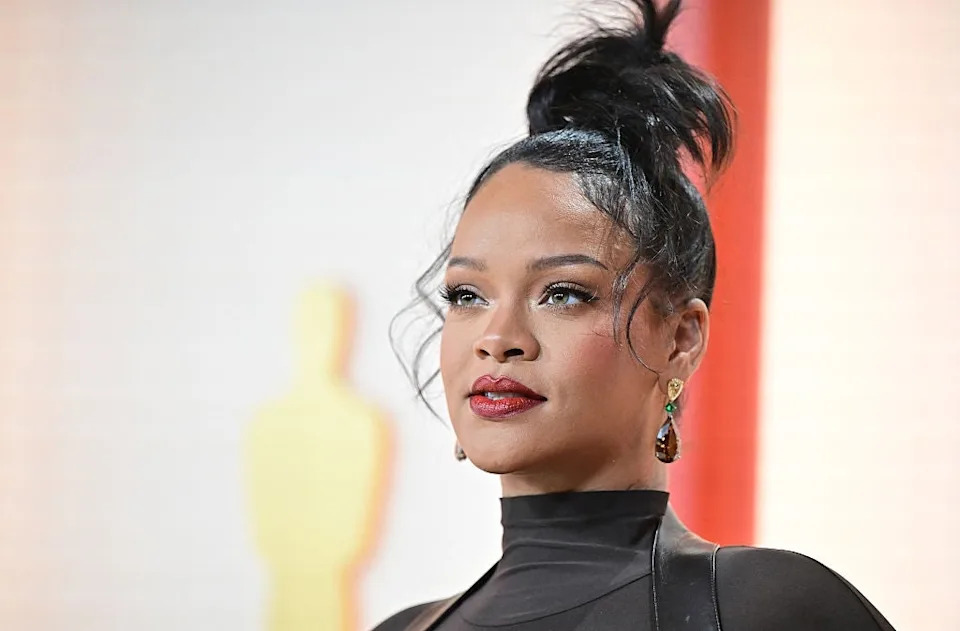 A person on a red carpet wearing an elegant, sheer black outfit and statement earrings, with hair styled in an updo