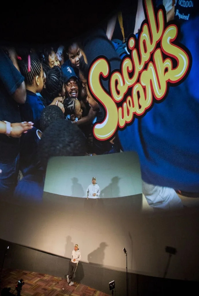 Person on stage at a SocialWorks event, with an image of people celebrating projected above