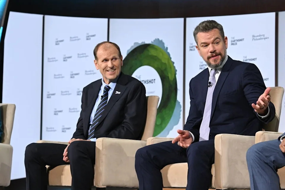 Two men in suits sit on a stage during a panel discussion at a sustainability-themed event