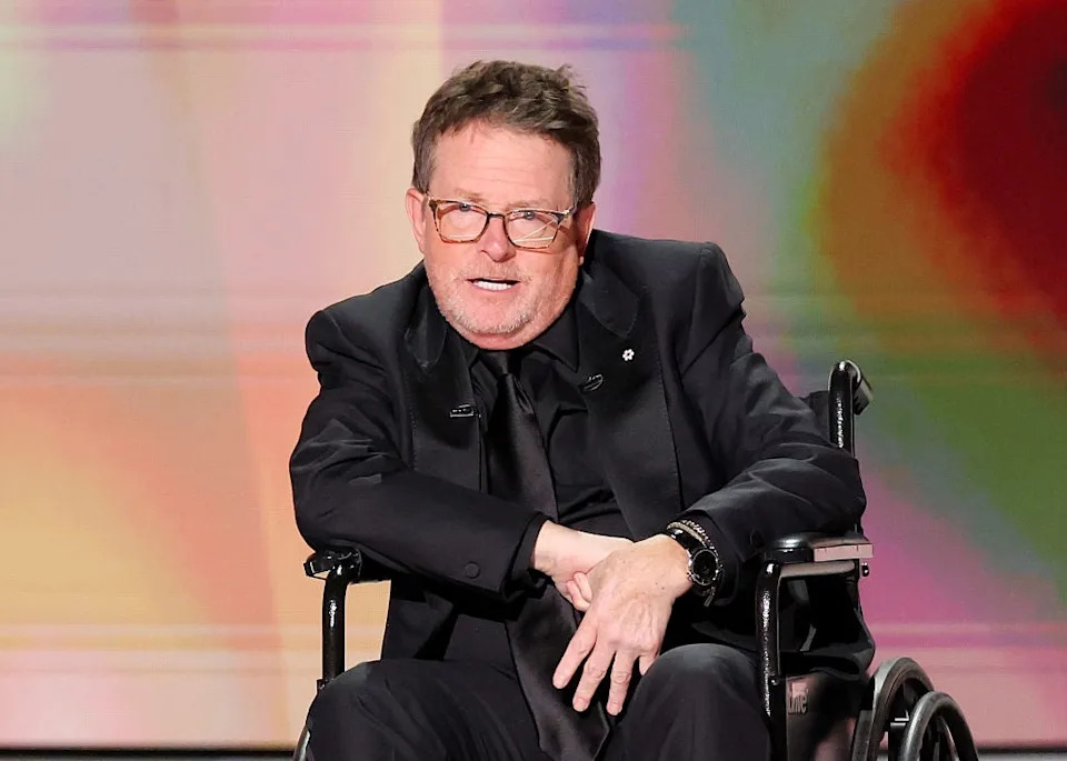 A person in a black suit speaks while seated in a wheelchair during an event