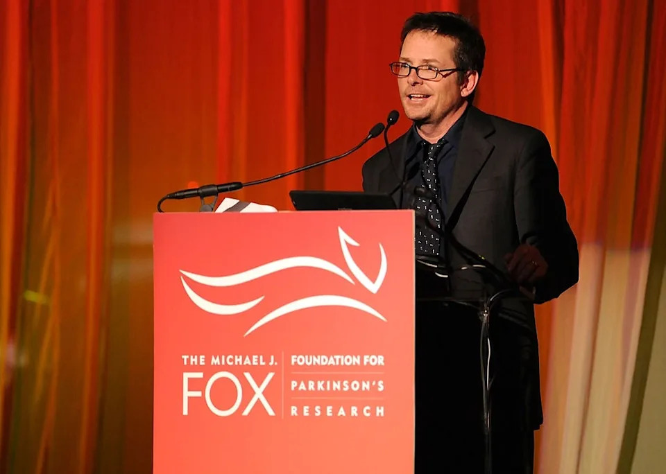 Man in a suit speaks at a podium for the Michael J. Fox Foundation event, focused on Parkinson's research