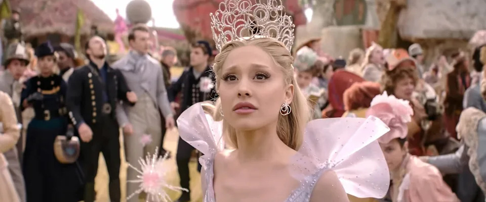 Person dressed in whimsical attire with a tiara and ruffled collar, part of a fantasy-themed gathering, looks ahead thoughtfully
