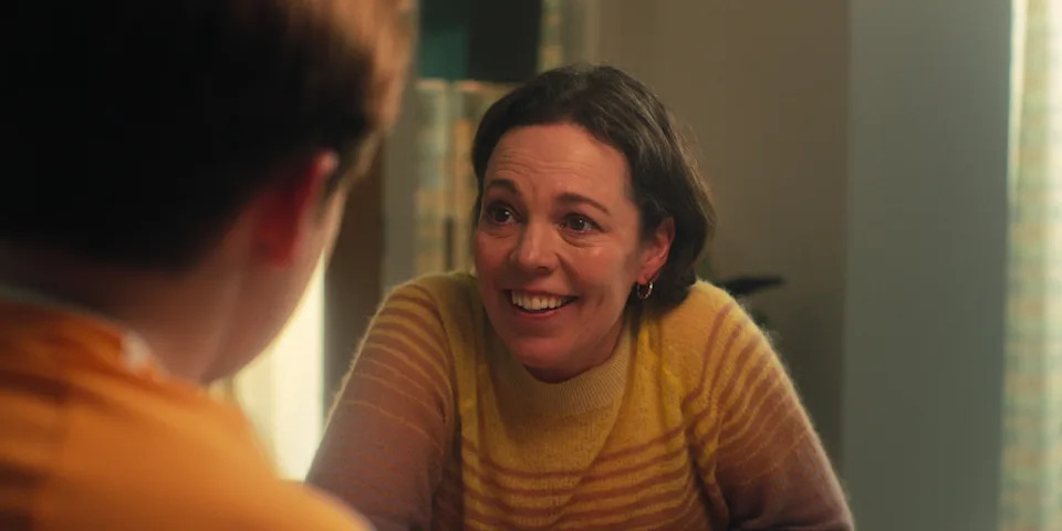 A person smiling warmly in a cozy setting, engaging with someone across from them