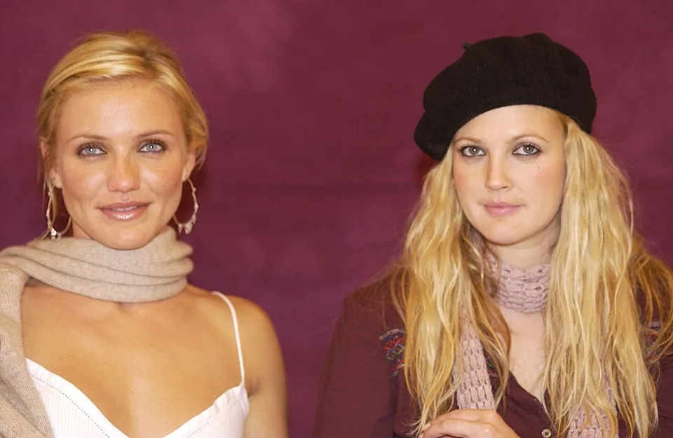 Two women are posing. One wears a white top and scarf, the other a black beret and scarf. Both have long hair and casual attire