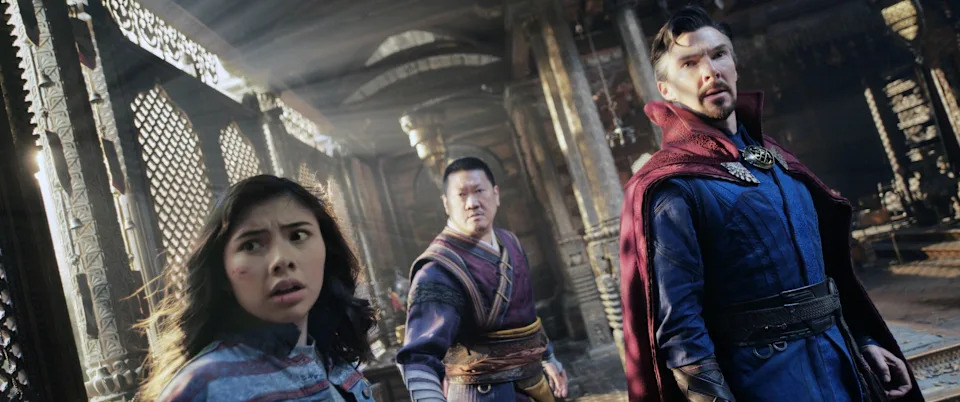 Three characters in action-ready poses in an ancient, mystical setting. One wears a cloak, another traditional robes, and the third a modern jacket