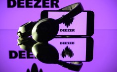 This photograph taken on January 13, 2025 in Toulouse shows headphones beside a smartphone and a computer screen displaying the logo of the French music streaming platform Deezer.