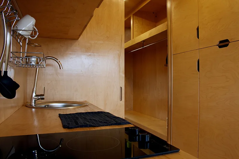 Innovative Birch Plywood Interior Transforms Shipping Container into Modern Micro-Cabin Kitchen seamlessly integrated into birch plywood wall design.