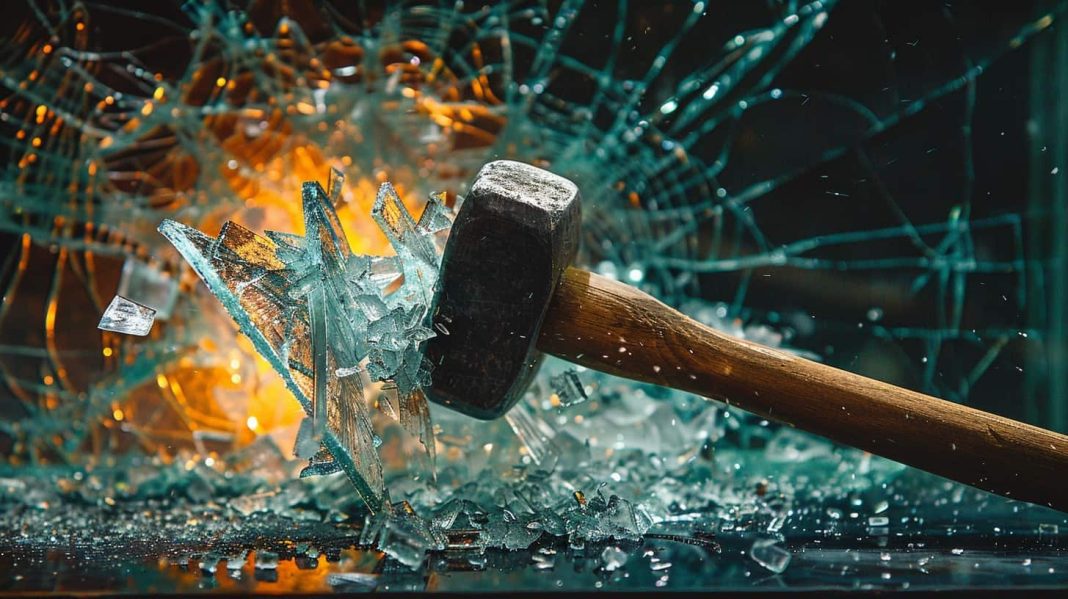 She’s Eyeing a $4,500 Mental Health Rage Retreat. Calling It Therapy Doesn’t Make It Medicare-Covered A close-up, high-speed photograph showing the head of a sledgehammer mid-impact as it shatters a pane of glass. Sharp, crystalline shards of glass explode outwards and fall onto a reflective surface below. The background is a dramatic, blurred blend of glowing orange and dark teal light, emphasizing the force and chaos of the breakage.