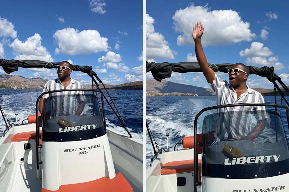 Person on a boat named "Liberty," smiling and waving, wearing sunglasses and a striped shirt, with a scenic ocean and mountain backdrop