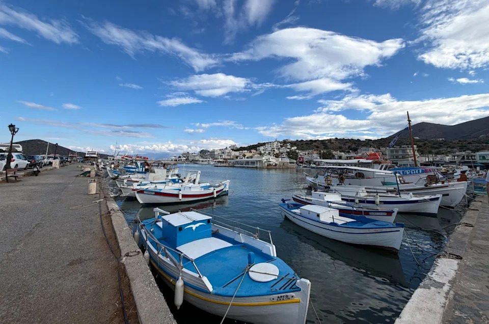 Fishing boats docked at a serene harbor with hills in the background and a partly cloudy sky