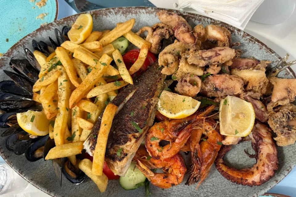 Platter of seafood including shrimp, mussels, grilled fish, fried calamari, and fries, garnished with lemon wedges and herbs