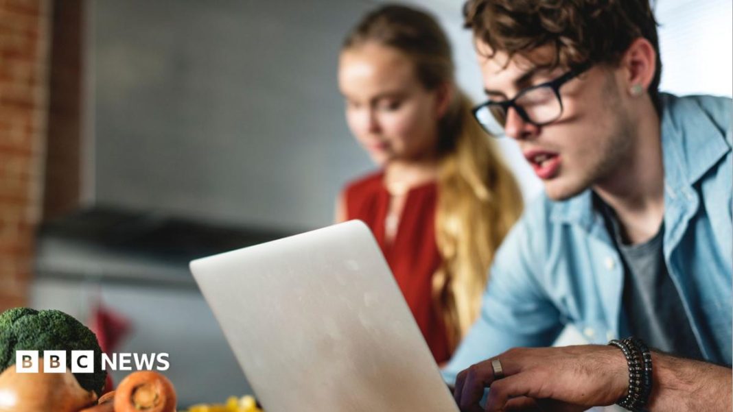 Your pay, energy bills and cash Isa: How the Budget affects you Man looks at laptop with a woman cooking behind him and some vegetables on a work surface behind the laptop.