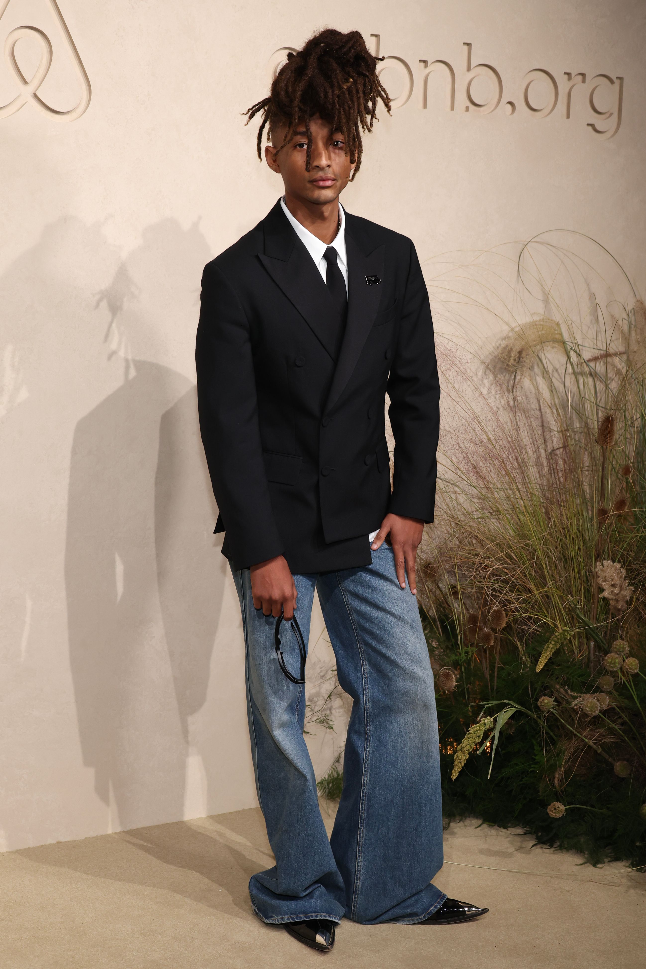 Jaden Smith poses on the red carpet wearing a black double-breasted blazer and loose blue jeans.