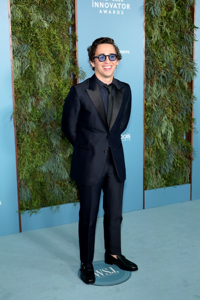 Marcello Hernández poses in a dark suit and tinted sunglasses at an awards event.