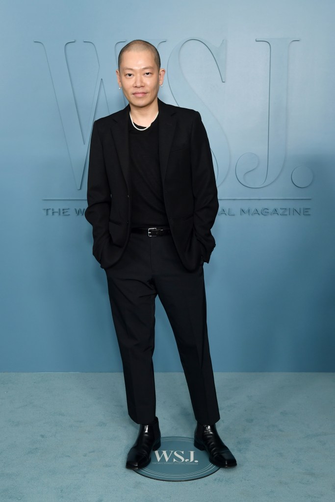 Jason Wu poses in a black suit and a pearl necklace on the blue carpet at the WSJ. Magazine Innovator Awards.