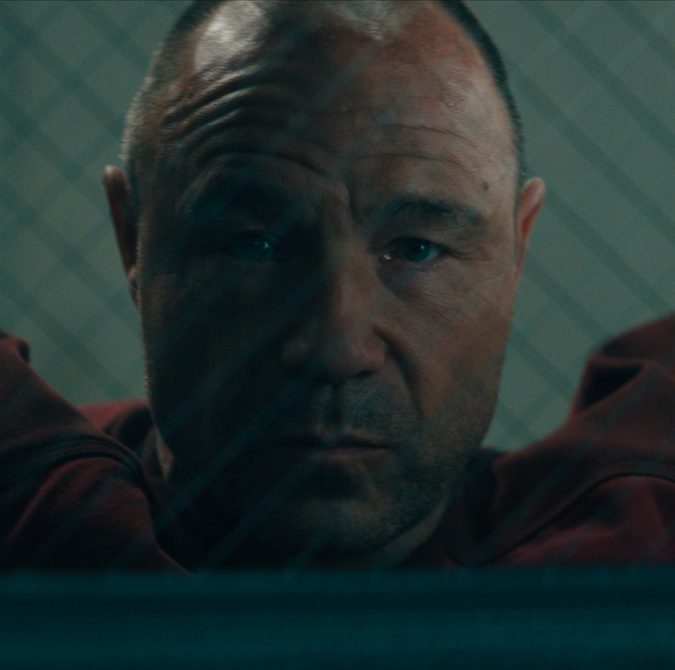 man with a scarred arm looks through a glass window with a grid pattern man with a scarred arm looks through a glass window with a grid pattern