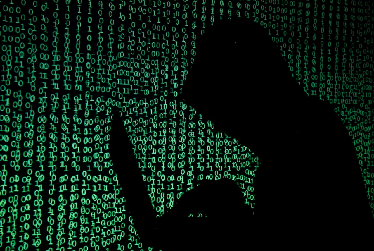 A silhouetted man hunched over a computer with data illuminated in the background.
