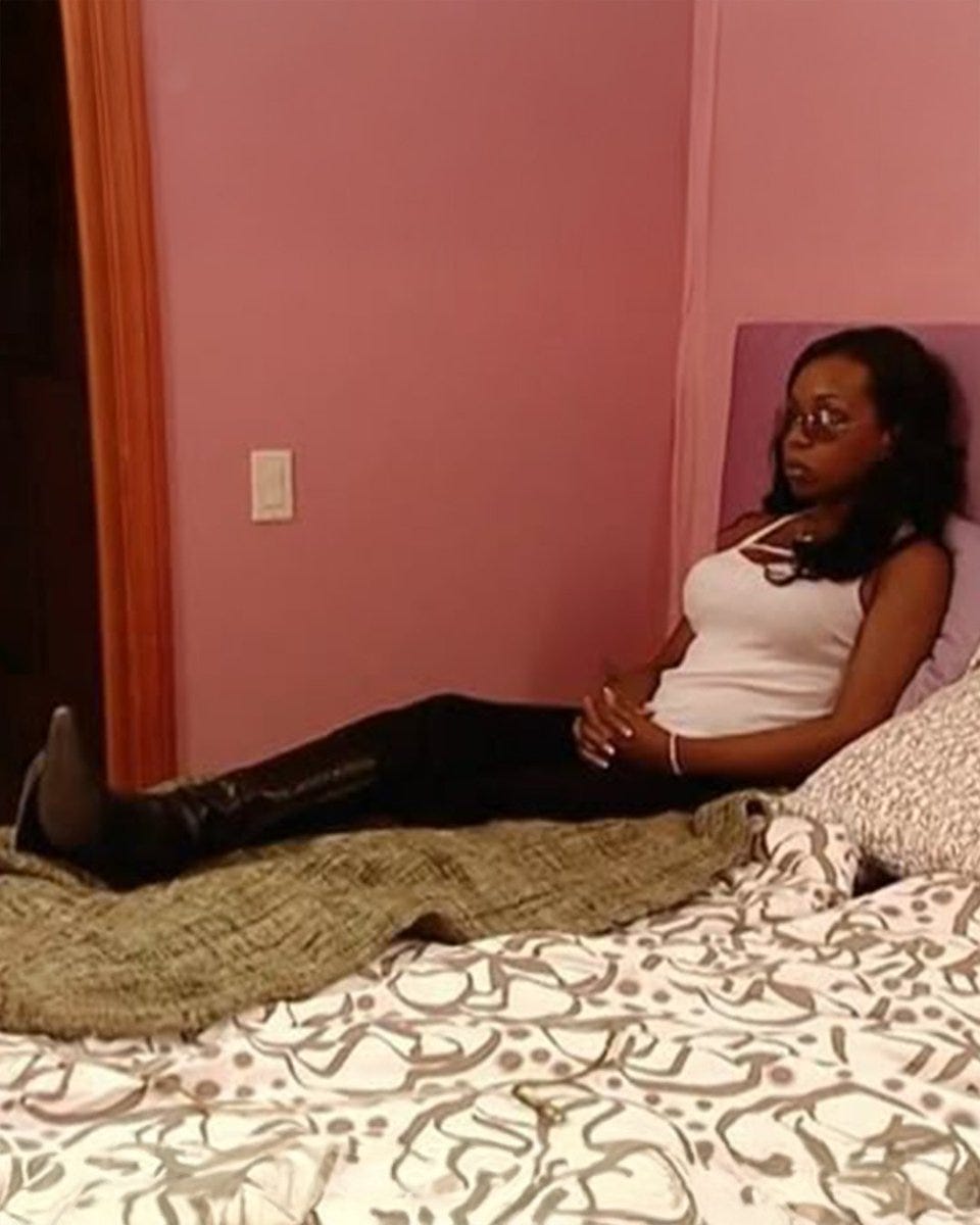 Person sitting on a bed in a pink room, looking contemplative. Person sitting on a bed in a pink room, looking contemplative.